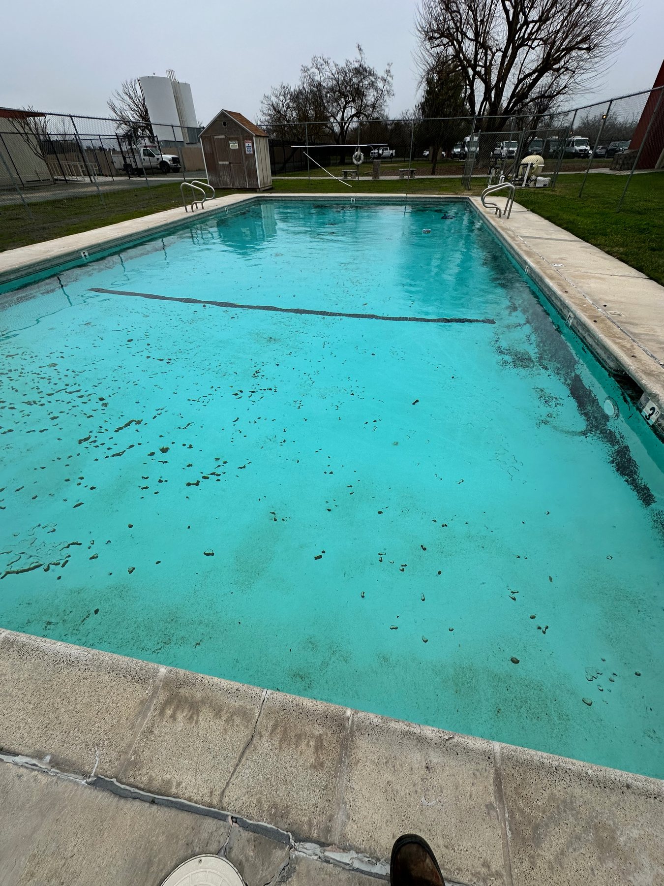 Outdoor pool with leaves and winter debris settled across the floor before seasonal cleaning.