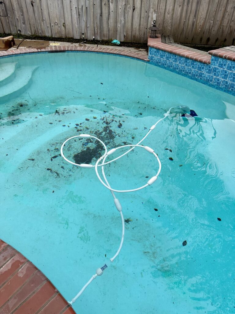 Suction-side pool cleaner hose surrounded by leaf debris